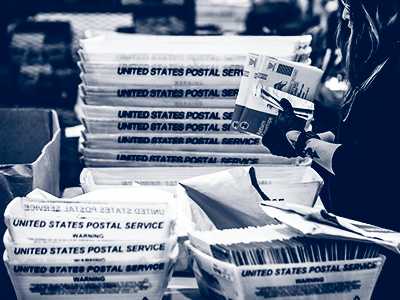 person holding ballots with stacks of mail bins